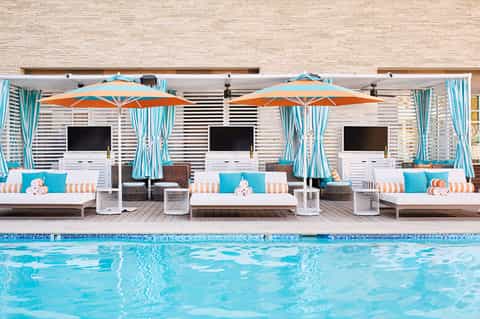 Luxury poolside lounge area with white daybeds, orange umbrellas, turquoise curtains and cabanas