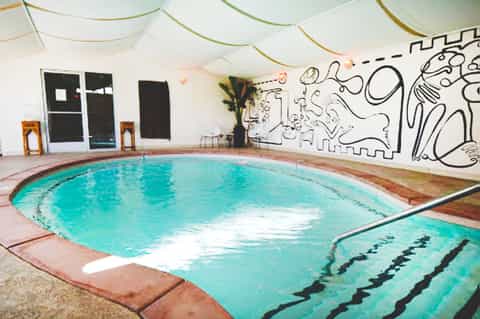 Indoor swimming pool with turquoise water, lane markers, and whimsical wall mural in converted warehouse space