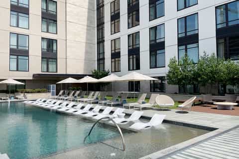 Contemporary hotel courtyard with modern pool, white lounge chairs, and umbrella shade