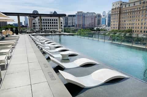 Modern white lounge chairs arranged along turquoise infinity pool with urban skyline and buildings