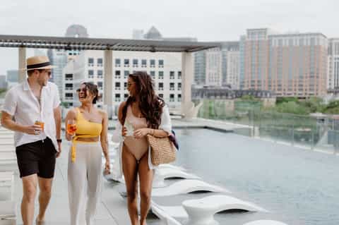 Urban rooftop terrace with three people, modern seating, pergola, river views, and downtown buildings