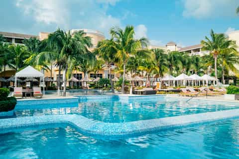Expansive luxury resort pool with white umbrellas, palm trees, and multi-story building