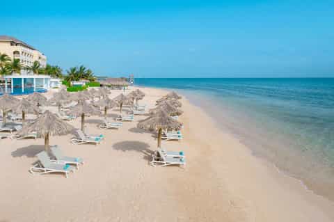 Sandy beach with thatched umbrellas, white lounge chairs, and turquoise ocean water