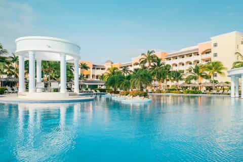 Large lazy river-style pool with white gazebo and colorful resort buildings surrounded by palms