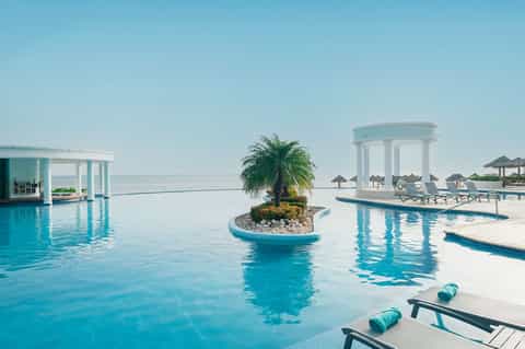 Infinity pool overlooking ocean horizon with white pergola and lounge chairs