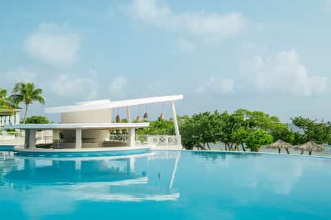 Luxury resort pool with modern white cabana structure and palm trees overlooking tropical waters