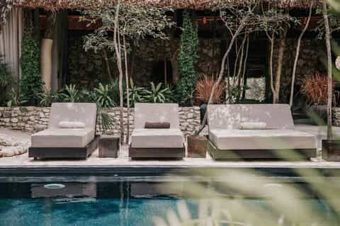 Luxury poolside loungers with stone wall backdrop and jungle-style landscaping
