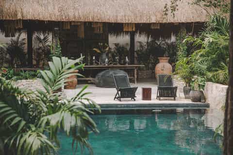 Tropical villa courtyard with thatched roof bar, pool, palm plants, and lounge seating area