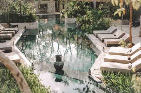 Serene courtyard pool with stone loungers, natural water feature, and lush plants