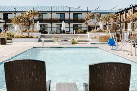 Contemporary hotel pool with white umbrellas, modern building facade, and golden grasses
