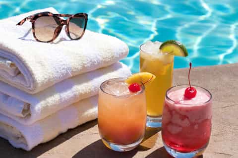 Poolside beverages with cherries and lime garnishes next to towels and sunglasses