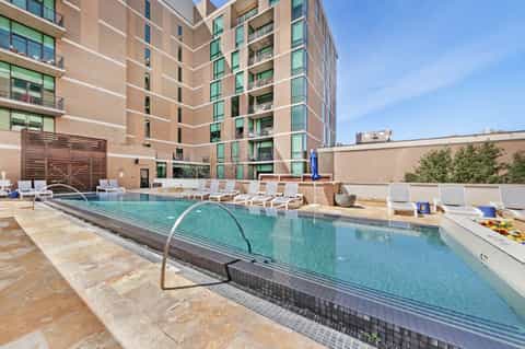 Urban hotel courtyard pool with turquoise water, white lounge chairs, and multi-story brick building backdrop