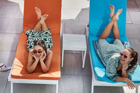Two women relaxing on colorful lounge chairs by the pool from overhead view