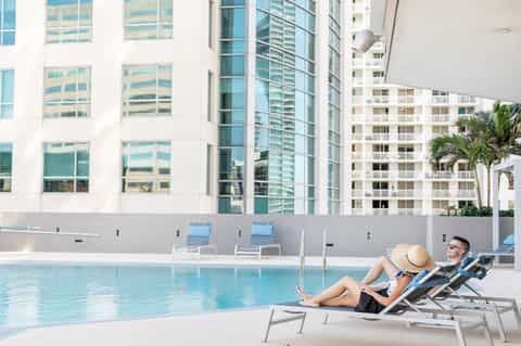 Urban hotel pool with two guests relaxing on loungers near modern buildings