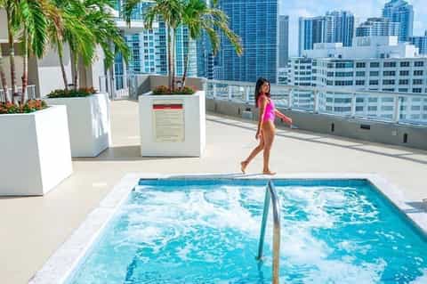 Woman in swimsuit on rooftop pool deck overlooking downtown cityscape