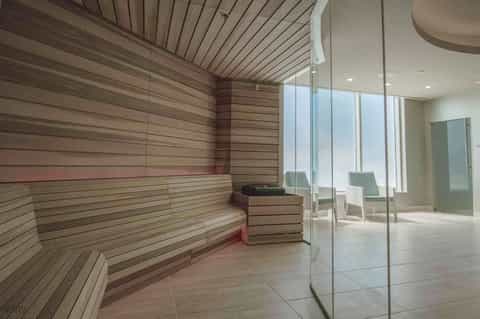 Sauna interior with wooden benches, glass door, and ocean view window overlooking terrace