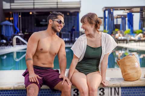 Couple relaxing by modern resort pool with blue umbrellas and contemporary architecture