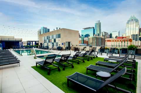 Rooftop pool deck with lounge chairs, cornhole games, and city skyline backdrop