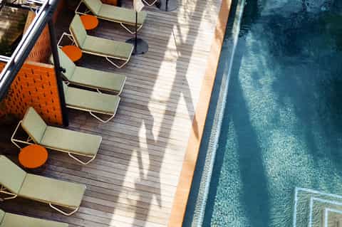 Aerial view of poolside lounge chairs with orange accents on wooden deck beside infinity pool