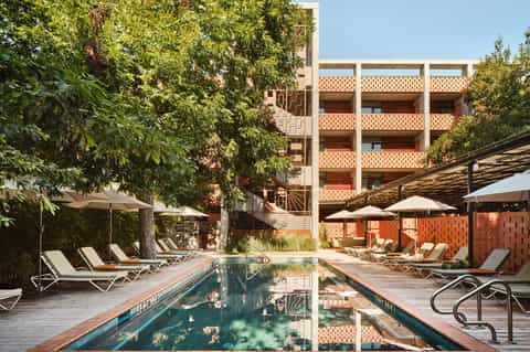 Courtyard pool surrounded by modern brick architecture, wooden loungers, umbrellas, and lush greenery