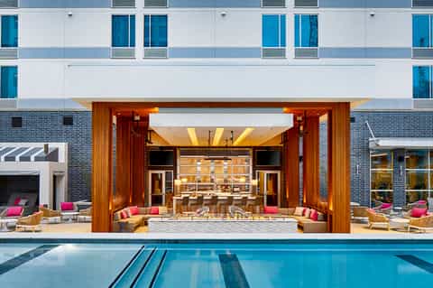 Modern hotel exterior with heated lap pool, wooden deck, and indoor lounge visible through glass doors