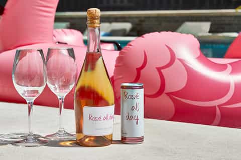 Rosé wine bottle and sparkling rosé can with empty glasses and pink floaties poolside