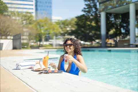 Woman in blue swimsuit relaxing poolside with book and beverage at resort pool