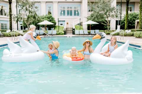 Family enjoying pool with giant swan floats and lounge chairs on white deck