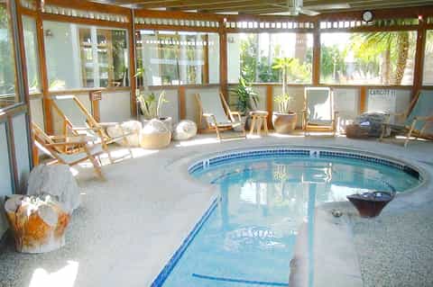 Indoor heated pool with lane dividers, wooden chairs, and palm plants visible