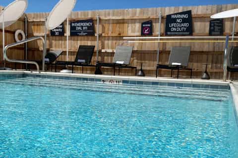 Outdoor pool with clear turquoise water, lounge chairs, and wooden privacy fence with safety signs