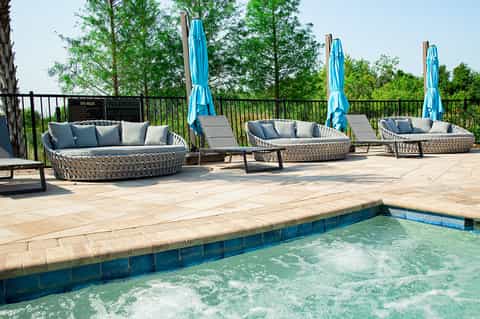 Outdoor resort patio with woven lounge seating, blue umbrellas, and spa pool area