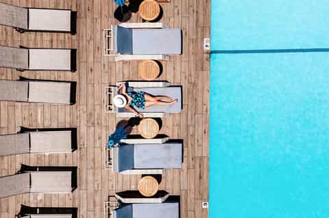 Aerial view of swimming pool deck with lounge chairs and sunbathers on wooden platform