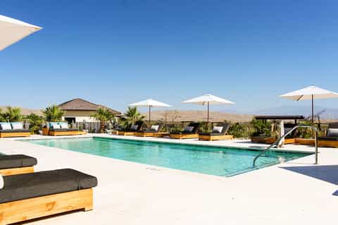 Desert resort pool with yellow loungers, white umbrellas, palms, and mountain landscape backdrop