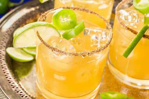 Golden cocktails with lime slices and spiced sugar rims on a decorative tray