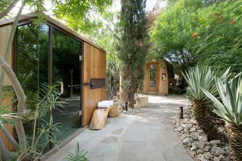 Modern spa treatment rooms with wood and glass doors nestled among lush green landscaping