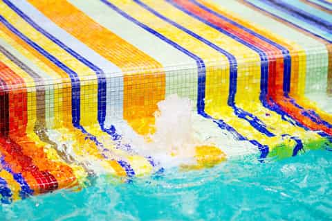 Swimmer doing freestyle stroke along colorful lane dividers in a competitive swimming pool