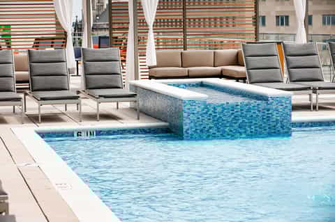 Resort pool with built-in spa feature, striped umbrellas, and modern lounge seating area