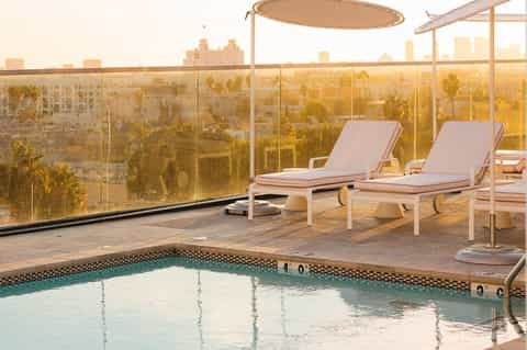 Rooftop terrace with lounge chairs, shade structures, and city skyline views at sunset