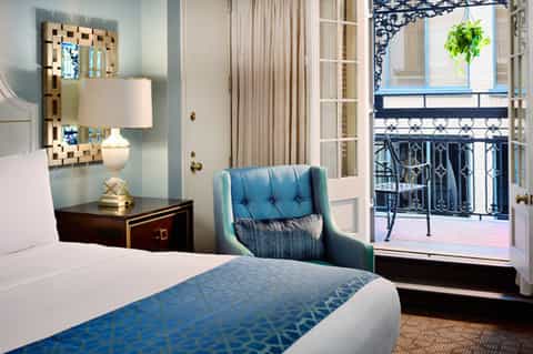 Hotel bedroom with blue accent chair, balcony, and elegant furnishings