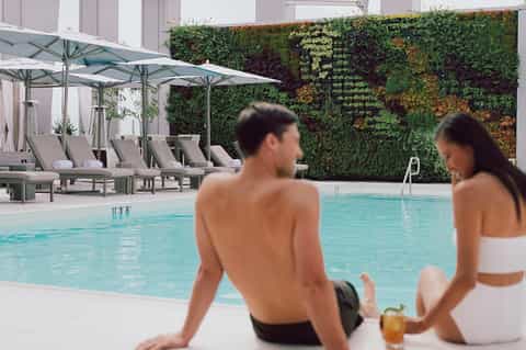 Resort poolside with loungers, umbrellas, living plant wall backdrop, and guests relaxing by water
