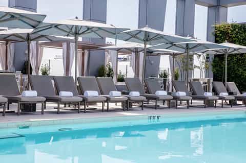 Modern pool deck with gray lounge chairs under umbrellas and a turquoise swimming pool