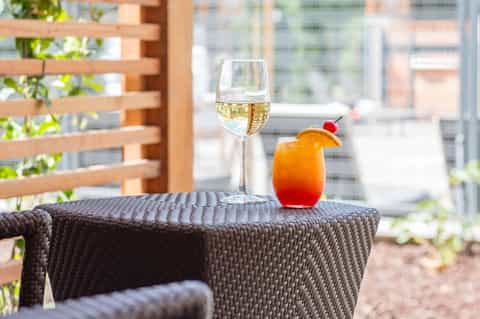 White wine glass and red cocktail with orange slice on a wicker table with city view