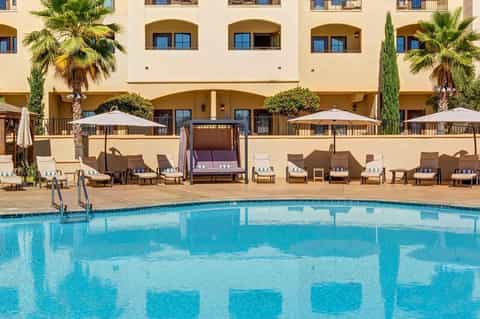 Resort pool with lounge chairs, umbrellas, and Mediterranean-style building facade