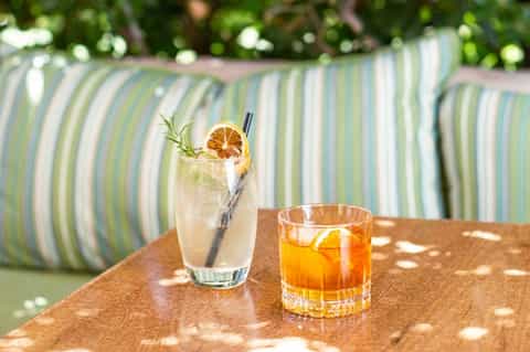 Two refreshing cocktails on wooden table with striped cushioned loungers in background