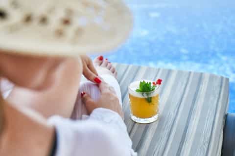 Woman relaxing poolside with tropical cocktail and ocean view in background