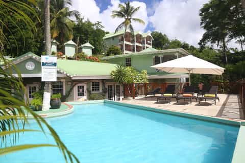 Resort pool surrounded by tropical vegetation with mint-green building and lounge area