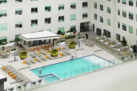 Aerial view of courtyard pool surrounded by white lounge chairs, yellow umbrellas, and hotel building