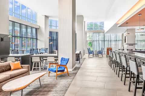 Modern hotel lobby lounge with dining area, kitchen, and large windows