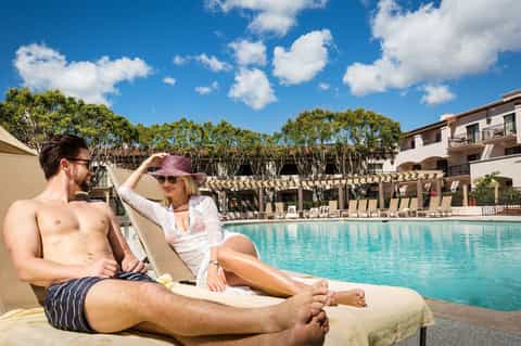 Couple relaxing on lounge chair by resort pool with manicured landscaping