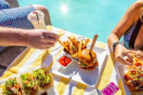 Couple enjoying poolside meal with burgers, fries, and cocktail by bright blue pool